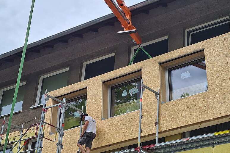 Bauarbeiter auf Gerüst mit schwebender Fassade vor Haus