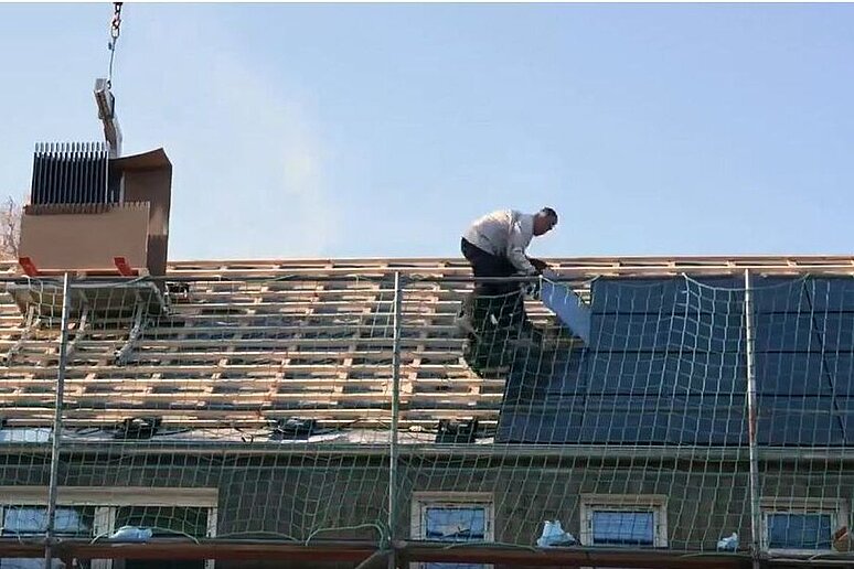 Arbeiter bringen PV-Module auf dem Dach eines Mehrfamilienhauses an