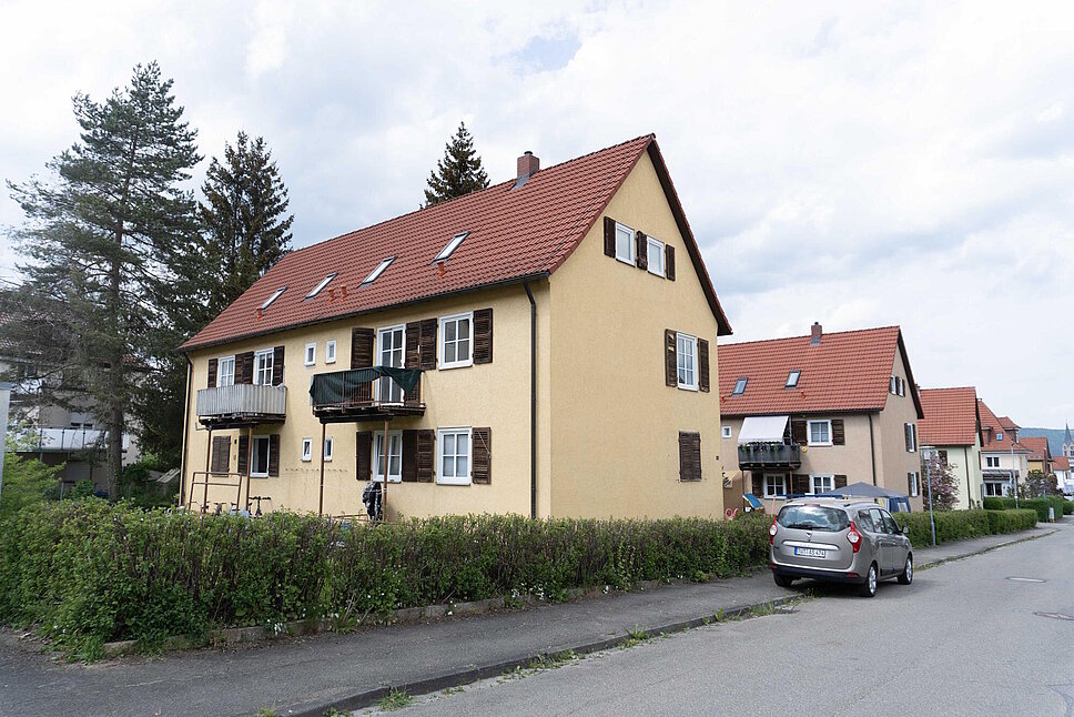 Mehrfamilienhaus mit Schrägdach vor Sanierung, davor eine Straße