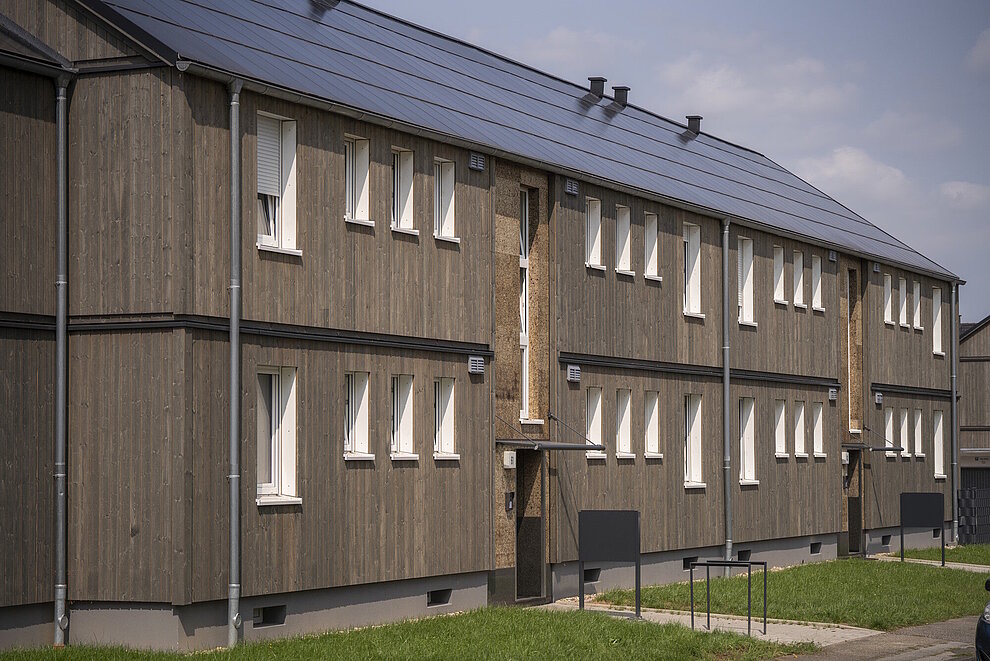 Saniertes Mehrfamilienhaus zweigeschossig mit dunkler Holzfassade, Schrägdach mit Photovoltaikanlage