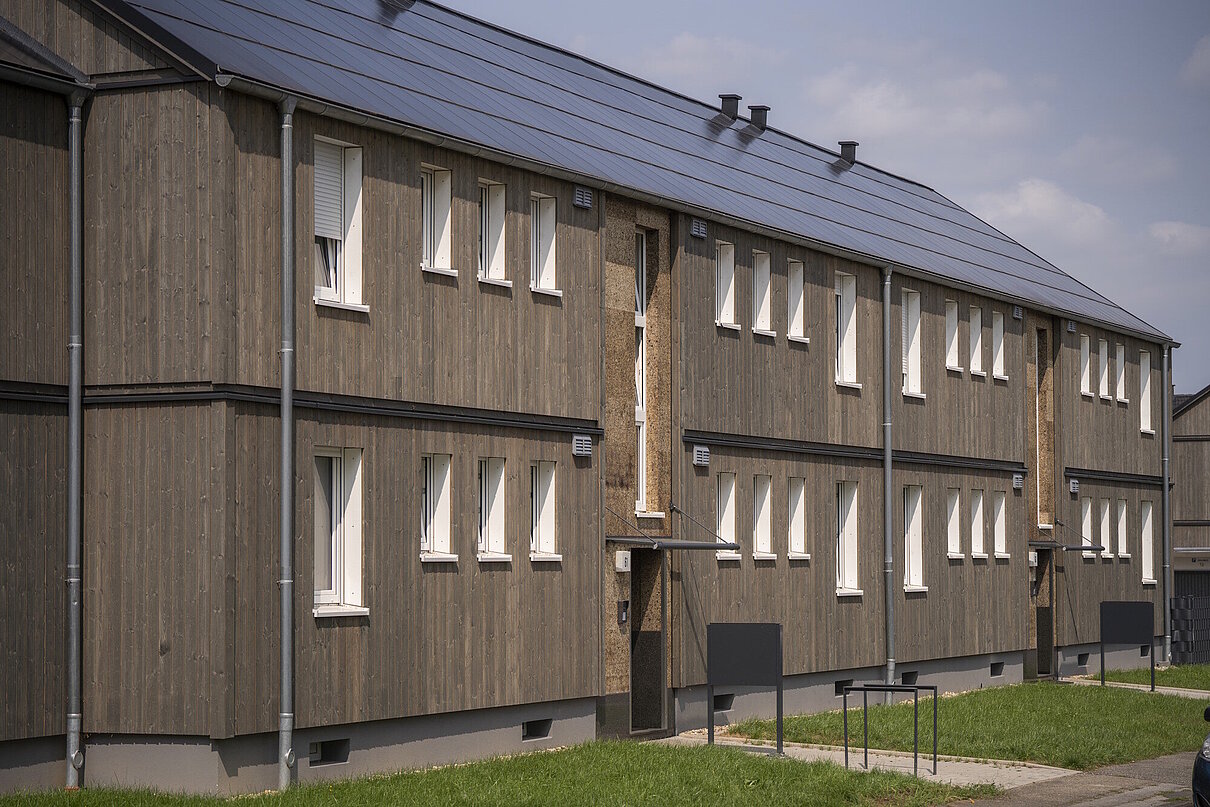 Saniertes Mehrfamilienhaus zweigeschossig mit dunkler Holzfassade, Schrägdach mit Photovoltaikanlage