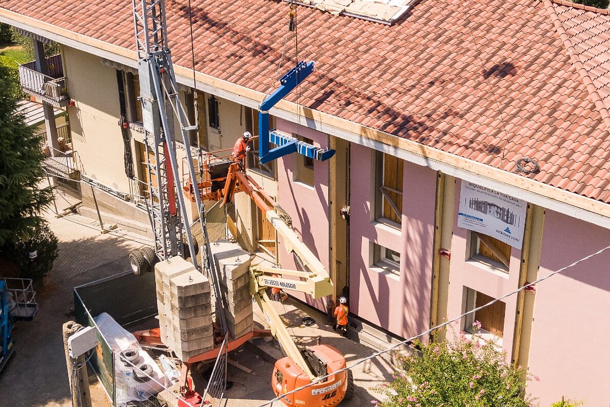 Mehrfamilienhaus in Italien während der Sanierung, davor ein Kran zur Montage der vorgefertigten Fassadenelemente