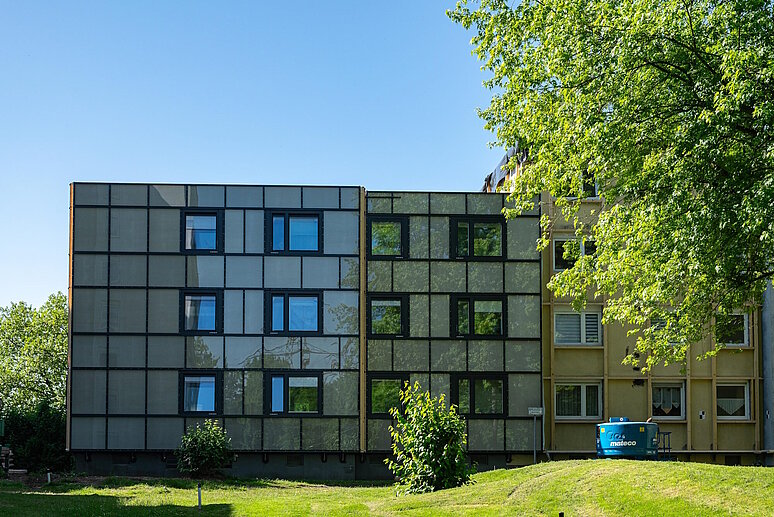 Frontansicht eines Mehrfamilienhause, davor Rasenfläche und ein Baum