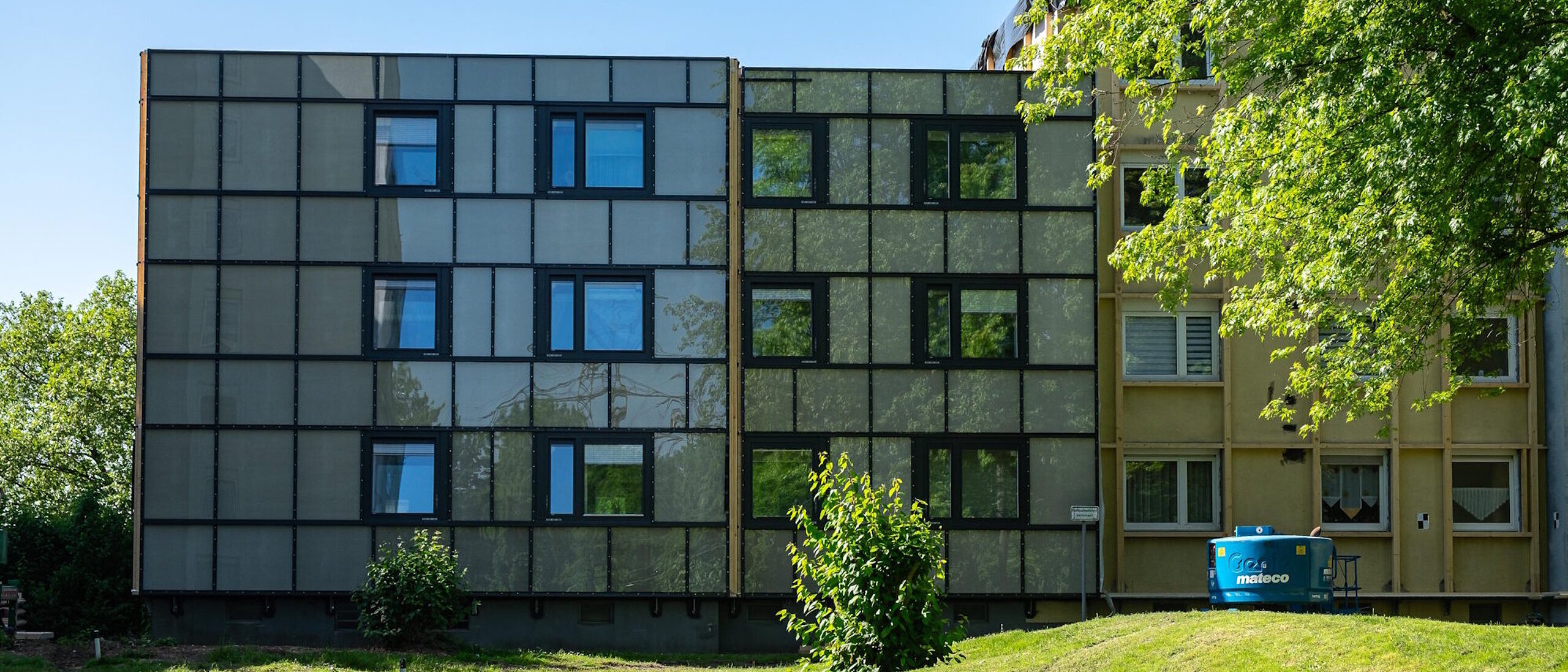 Frontansicht eines Mehrfamilienhause, davor Rasenfläche und ein Baum