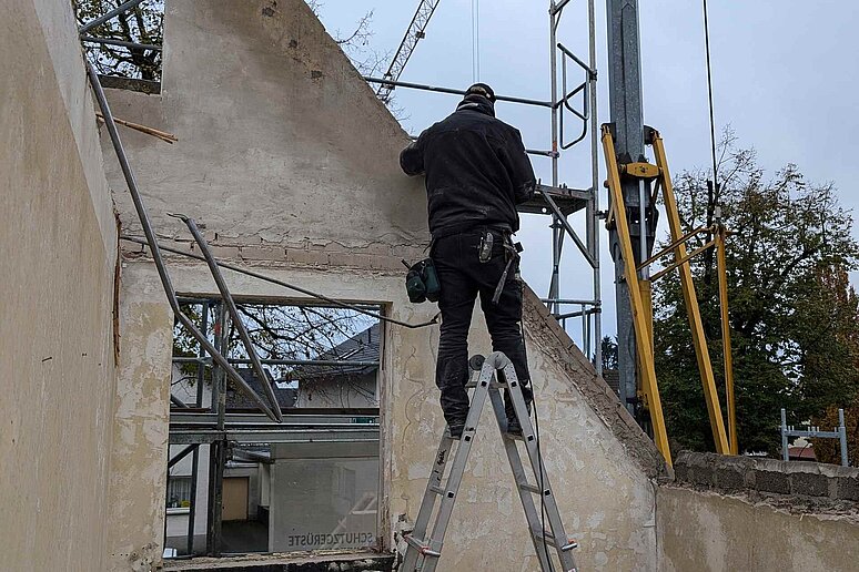 Bauarbeiter mit Kran an Haus mit Leiter