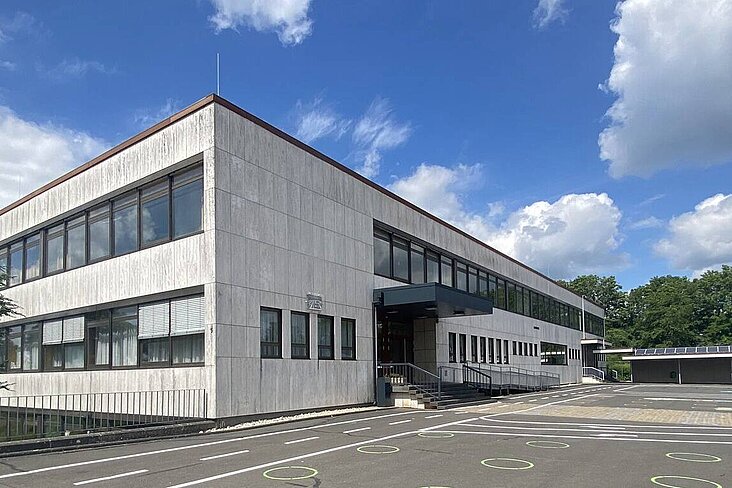 Unsaniertes Schulgebäude und Schulhof, blauer Himmel mit dicken weißen Wolken