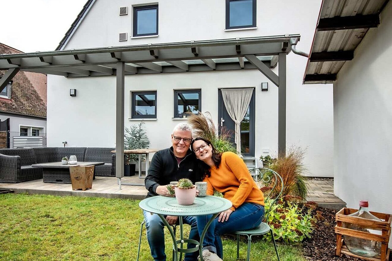 Ehepaar am Tisch im Garten vor Einfamilienhaus