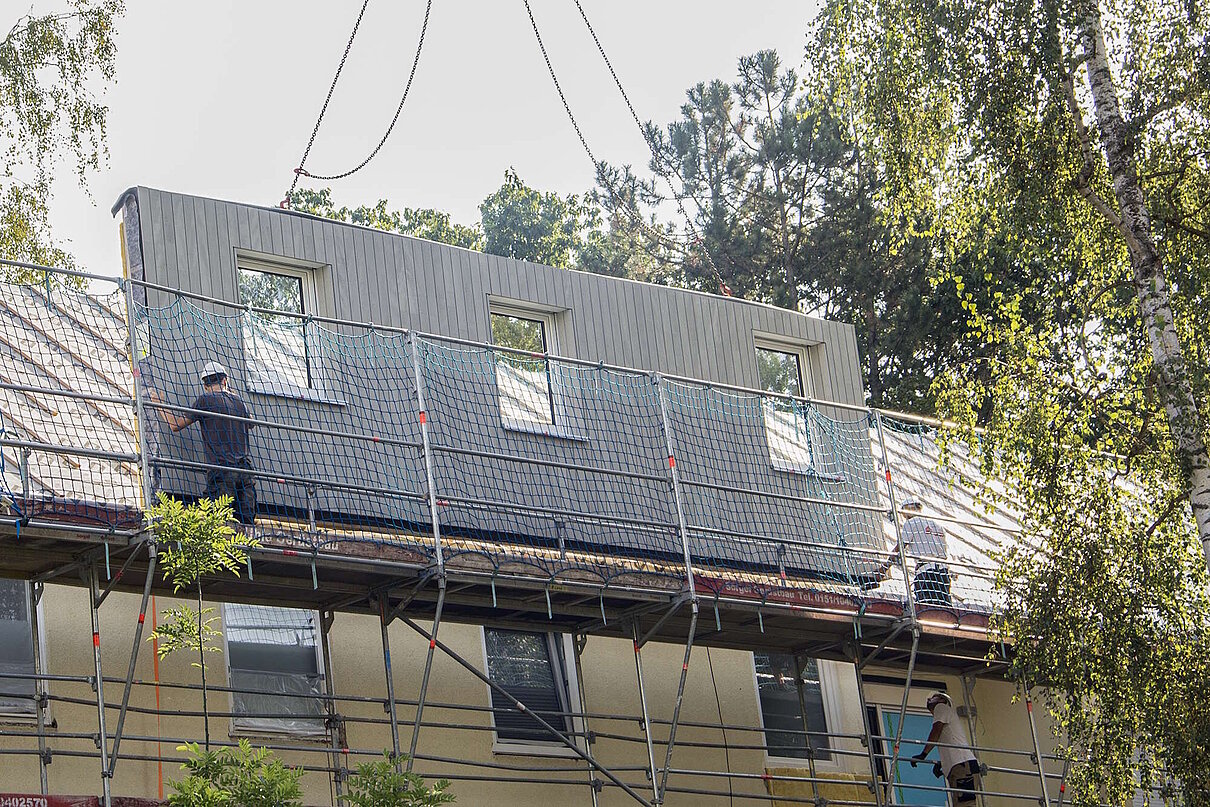 Vorgefertigtes Fassadenelement wird von Bauarbeitern für Montage am Haus platziert.