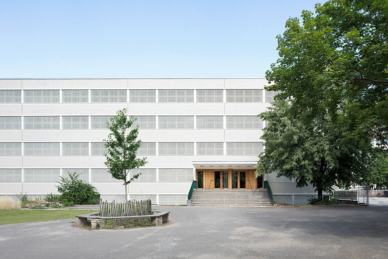 Saniertes Schulgebäude viergeschossig, davor Schulhof und Baum 