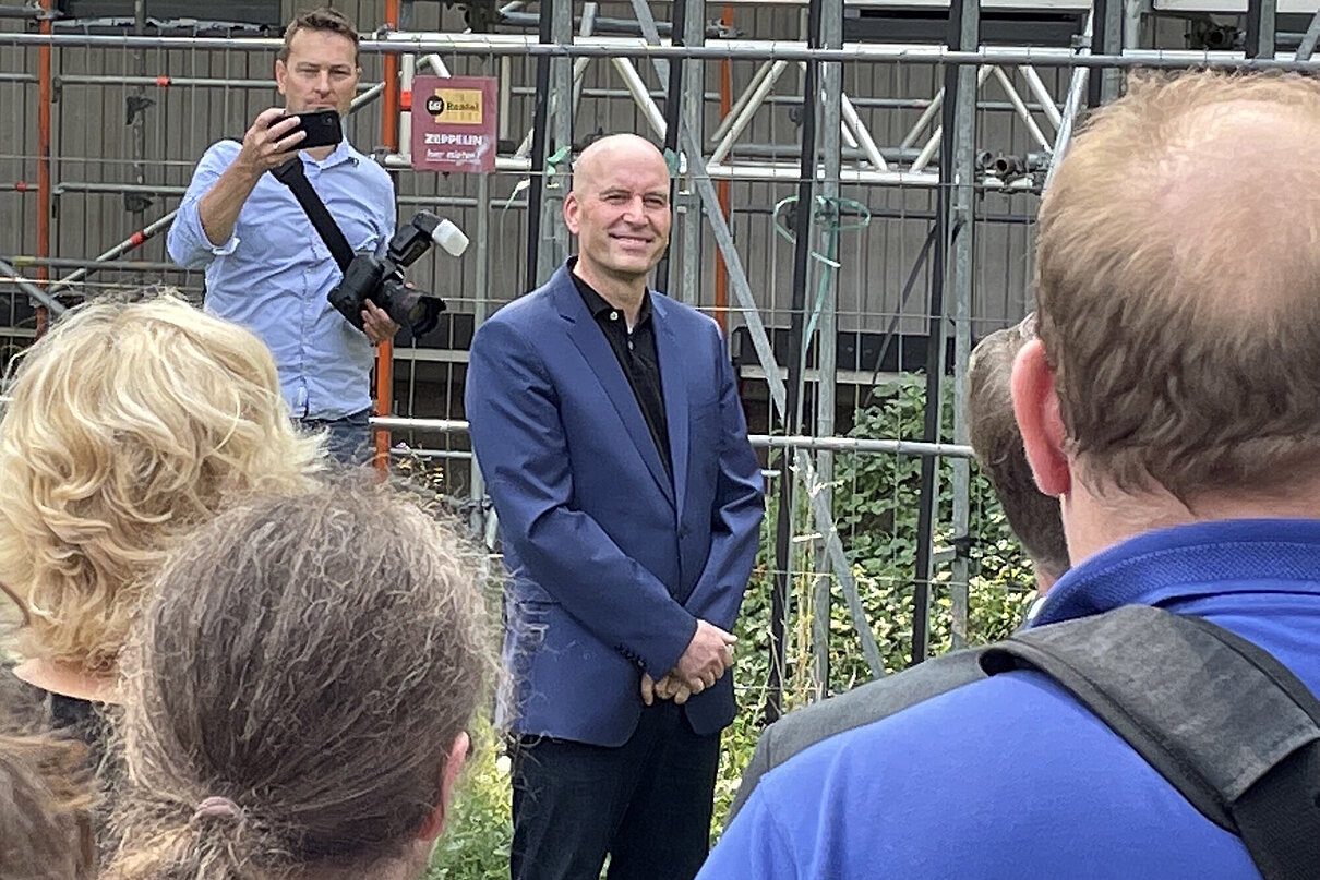 Personen schauen auf eine Person in der Mitte, im Hintergrund eine Person mit Fotokamera