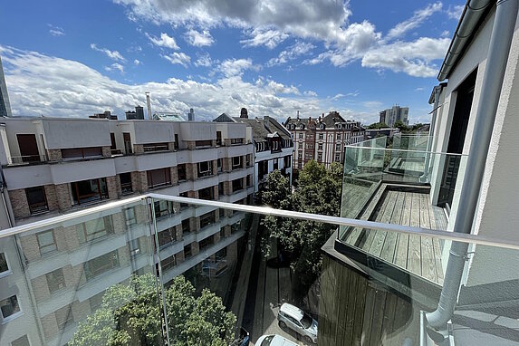 Blick von einem Balkon auf ein gegenüberstehendes Mehrfamilienhaus, blauer Himmel mit vielen weißen Wolken