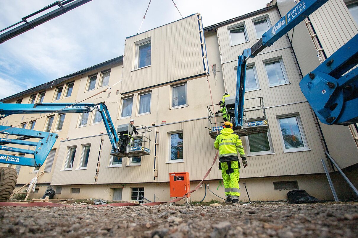 Arbeiter bringen per Kran vorgefertigte Fassadenteile an Gebäude an