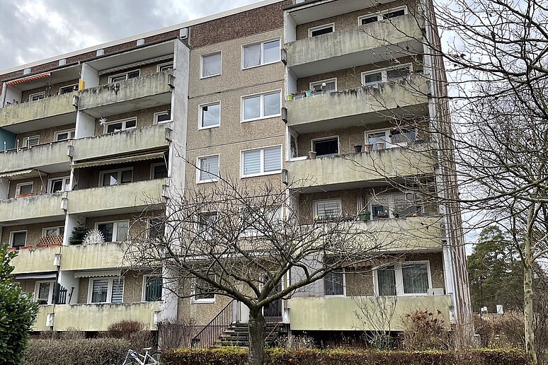 Plattenbau mit Balkonen unsaniert, Bäume und Sträucher