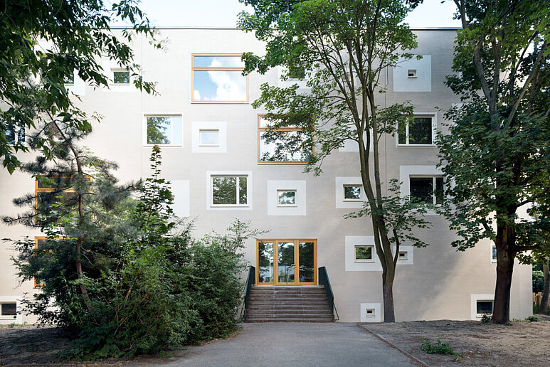 saniertes Gebäude mit heller Fassade und Fenstern, davor Laubbäume