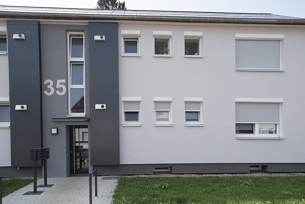 Saniertes Mehrfamilienhaus zweigeschossig, helle Fassade, Eingangsbereich in dunkelgrau gestaltet