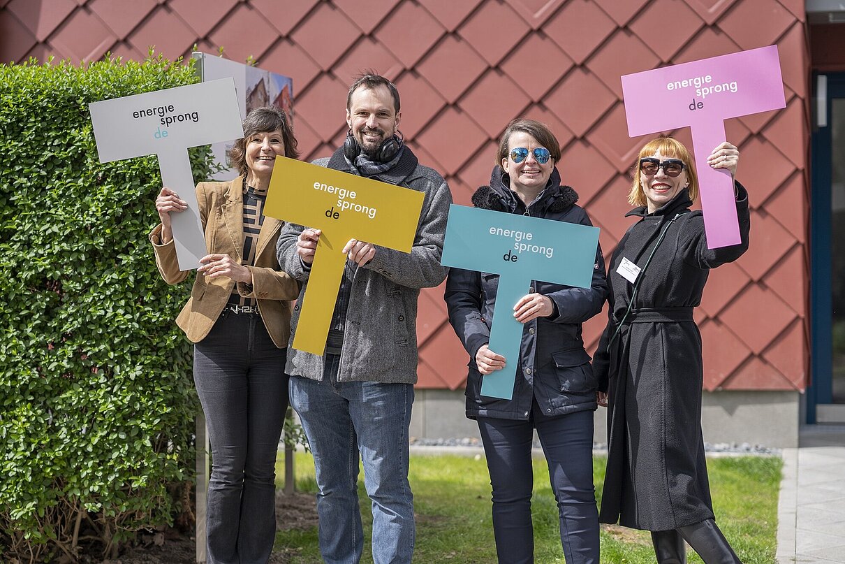 Vier personen stehen nebeneinander mit je einem farbigen Schild in der Hand mit dem Aufdruck "energiesprong.de".