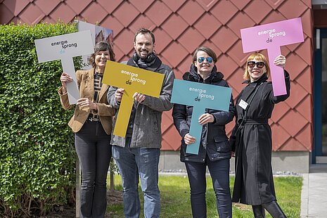 Vier personen stehen nebeneinander mit je einem farbigen Schild in der Hand mit dem Aufdruck "energiesprong.de".