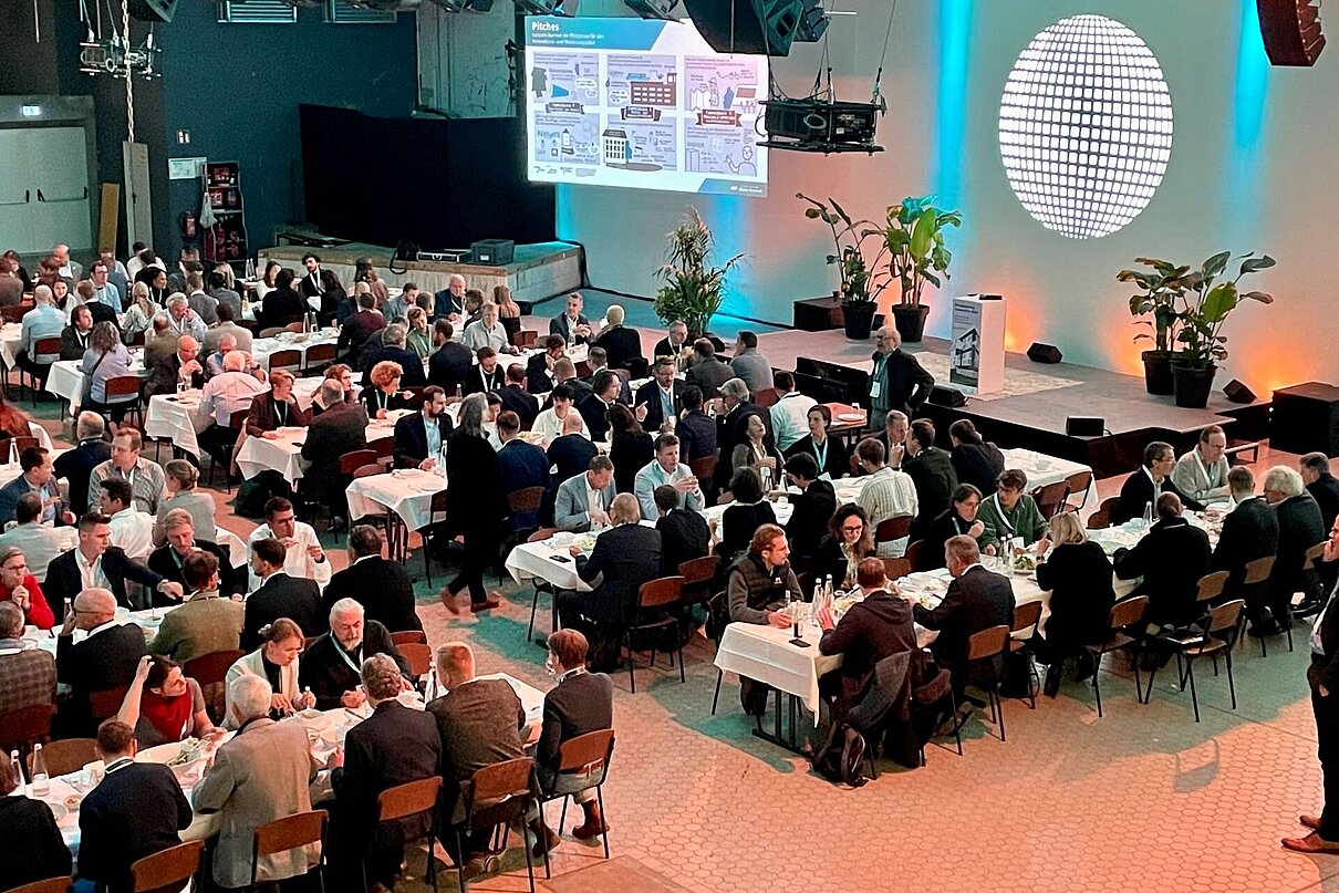 Viele Menschen an Tischen beim Essen in großer beleuchteter Halle