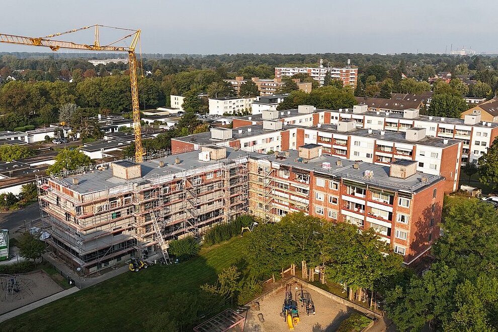 Blick von oben auf einen Wohnkomplex, der saniert wird. Drumherum sind Grünflächen und Bäume.