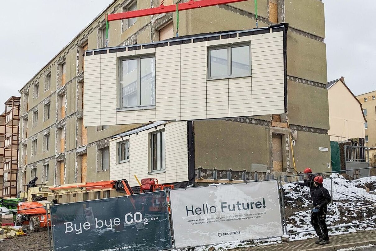 Fassadenelement schwebt vor einem Mehrfamilienhaus.