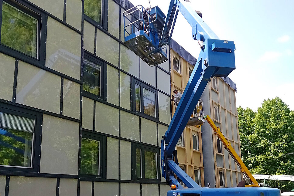 Montage eines Fassadenelements an ein Mehrfamilienhaus mit Hilfe eines Kranfahrzeugs