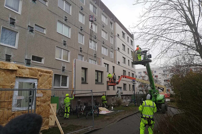 Plattenbau während serieller Sanierung mit vorgefertigten Fassadenelementen, Bauarbeiter in Schutzkleidung