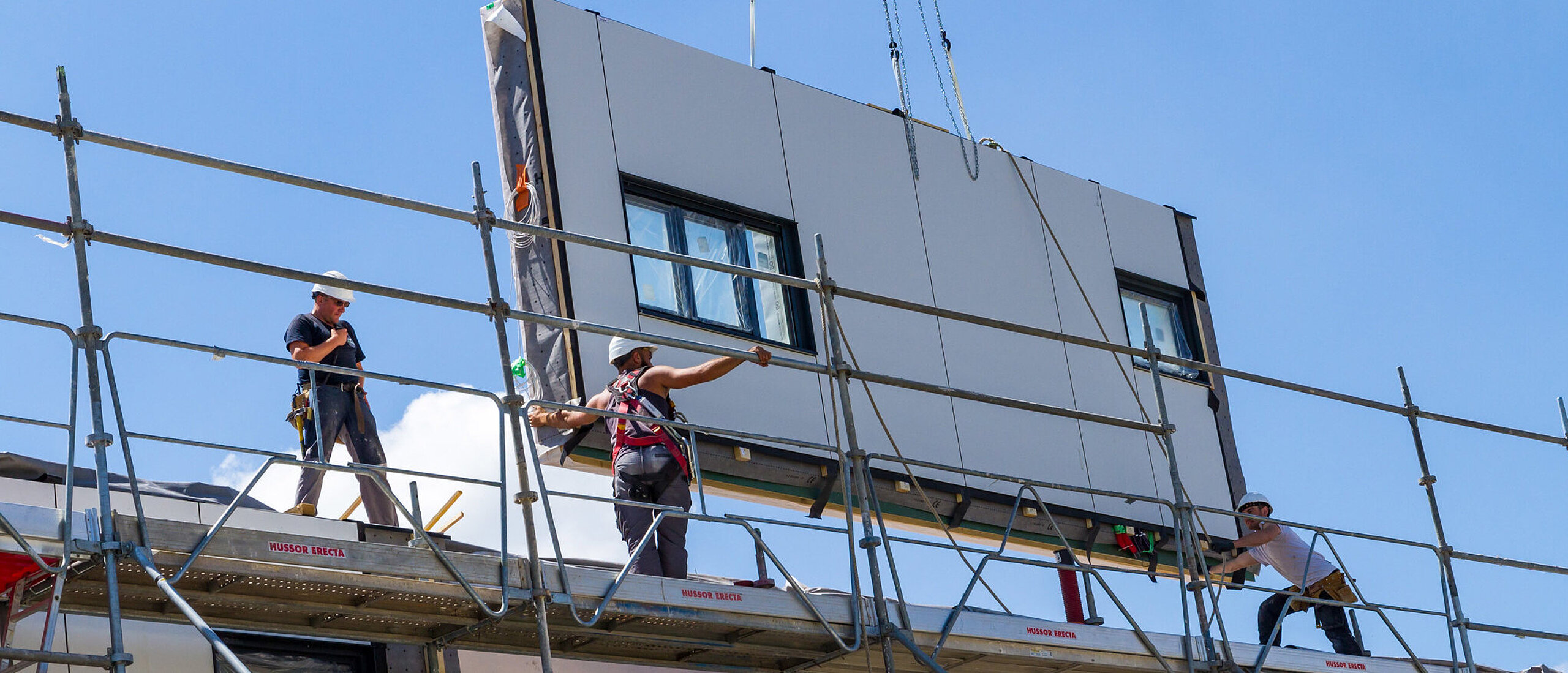 Hausfassadenelement mit Fenstern wird von Bauarbeitern zur Montage platziert.